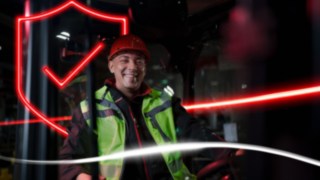 Työvaatteisiin ja suojakypärään pukeutunut henkilö istuu Linde-haarukkatrukissa Työvaatteisiin ja suojakypärään pukeutunut henkilö istuu Linde-haarukkatrukissa