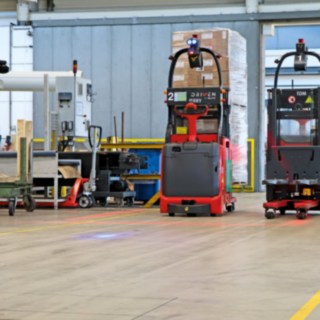 Kaksi automaattista L-MATIC-pinontatrukkia kuljettaa tavaroita pakkauslinjan ja dynaamisen varaston välillä.